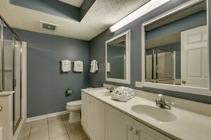 A bathroom with two sinks, a toilet, and a shower. There are towels hanging on the wall and a mirror above the sink.
