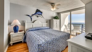 A bedroom with a bed, a nightstand, a ceiling fan, a window with a view, and a desk. - Ashworth by Condo-World (North Myrtle Beach)