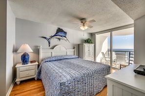 A bedroom with a bed, a nightstand, a ceiling fan, a window with a view, and a desk.