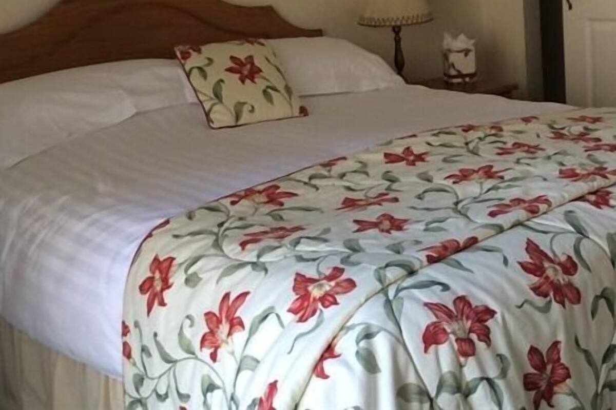 A bed with a floral bedspread, a wooden headboard, and a nightstand with a lamp.