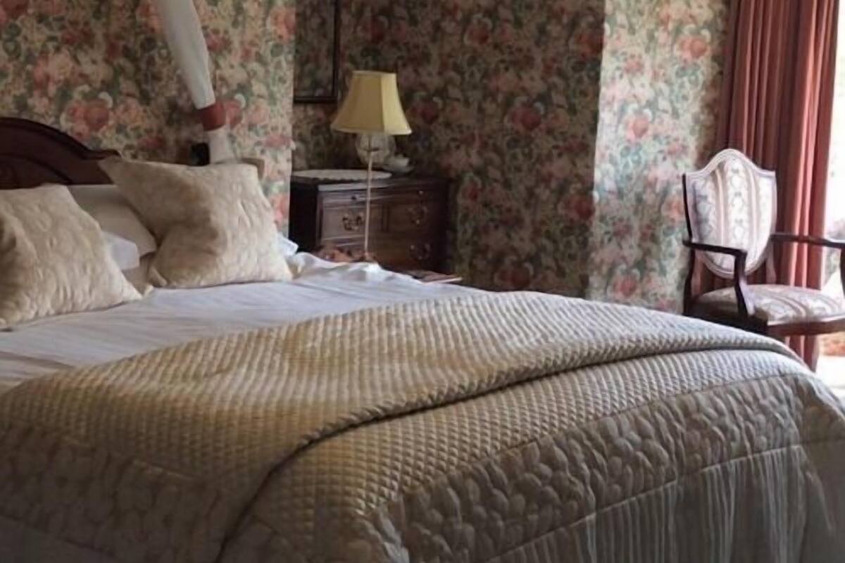 A bedroom with a bed, pillows, a nightstand, a lamp, and a chair.