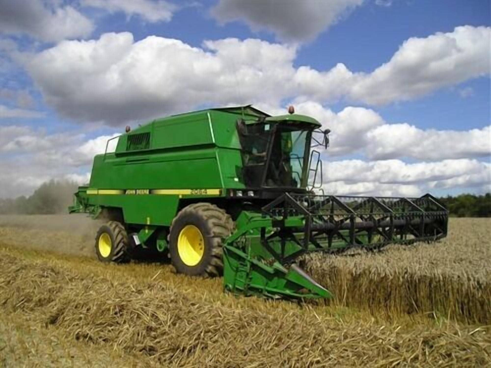 A green combine harvester in a field with a clear sky and clouds.