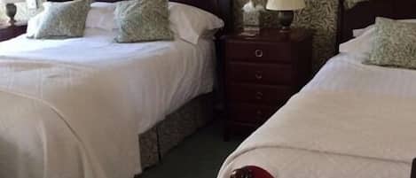 A hotel room with two beds, each with white bedding and decorative pillows. There is a wooden nightstand with a lamp between the beds.