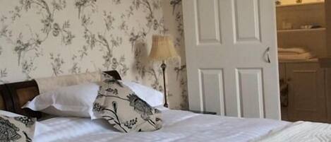 A bedroom with a bed, floral wallpaper, a nightstand, and a door leading to a bathroom.