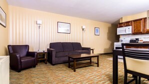 Ein Hotelzimmer mit Wohnbereich, ausgestattet mit einer Couch, einem Sessel, einem Couchtisch und einem Esstisch mit Stühlen. In der Küchenzeile sind eine Mikrowelle und ein Herd zu sehen.