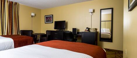 A hotel room with two beds, a desk, a television, a mirror, and a window with curtains.