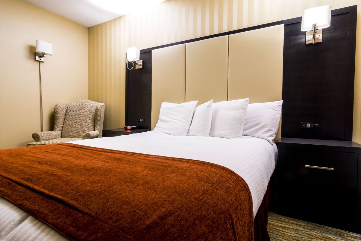 A hotel room with a large bed, a bedside table, a chair, and a nightstand.