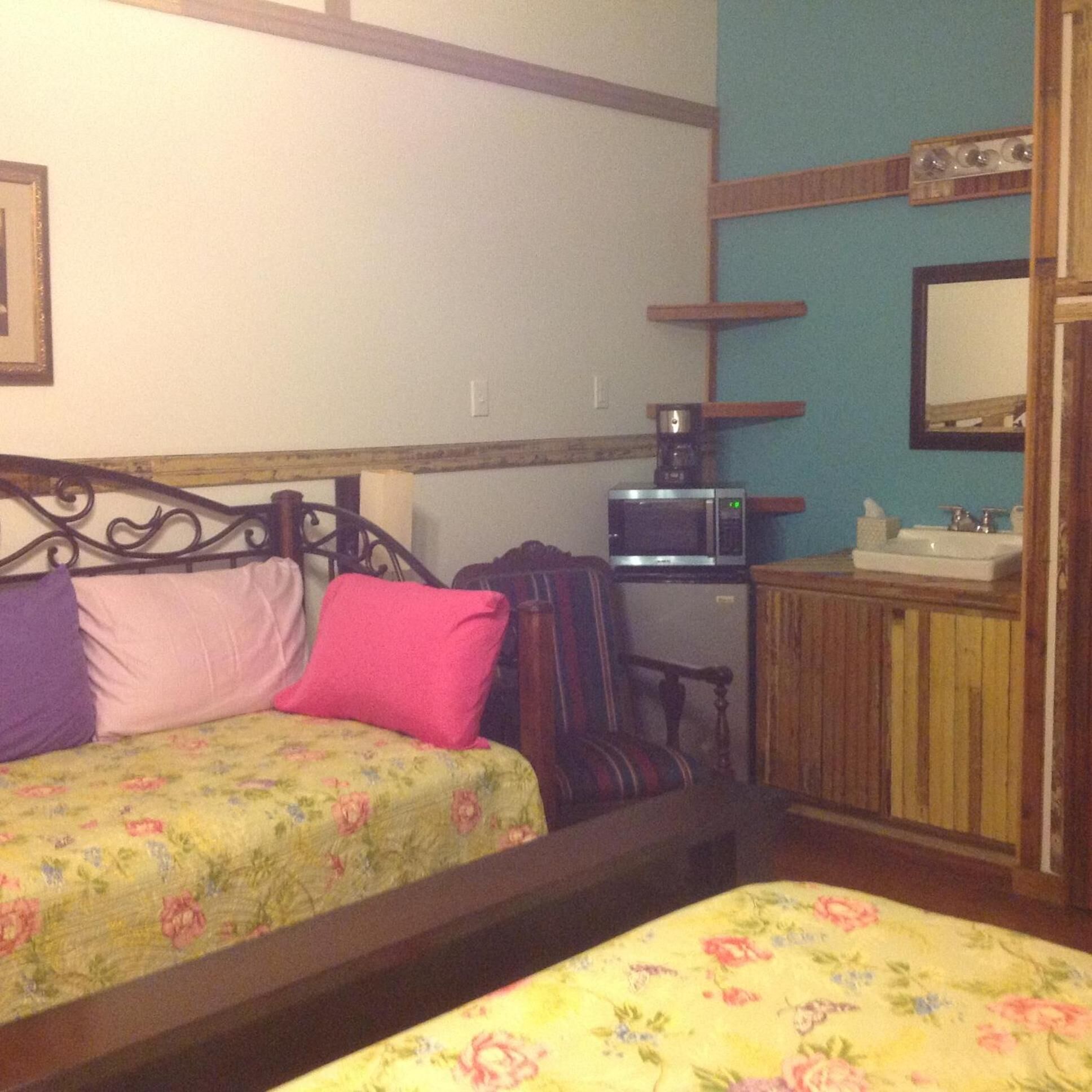 Un dormitorio con dos camas individuales, cabecero de madera, un escritorio pequeño con microondas, un armario de madera y un espejo en la pared.