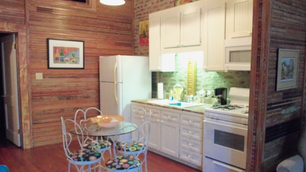Una cocina compacta con gabinetes blancos, un refrigerador, una estufa y una mesa de comedor con sillas.