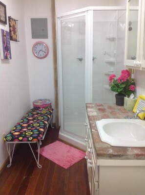 A bathroom with a shower, a sink, a small bench, a clock, and a potted plant. - The Main Street Hotel (Yazoo City)