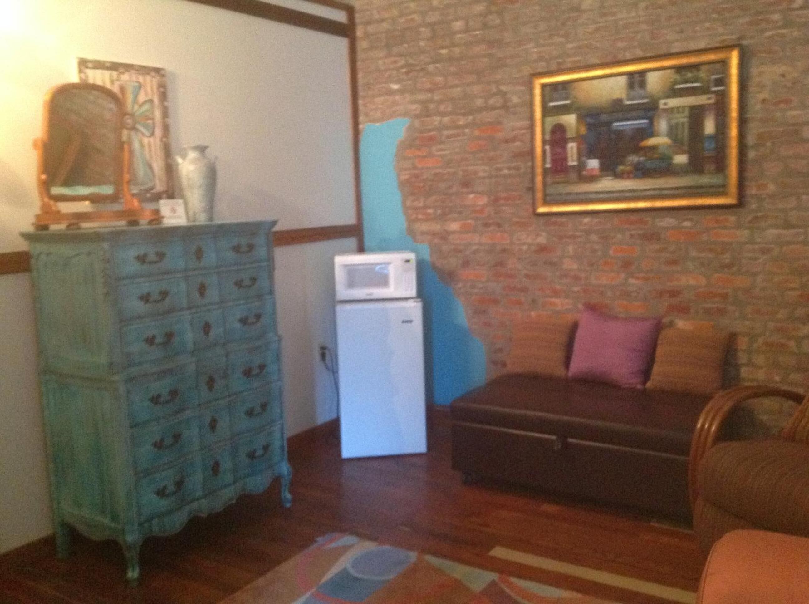 Una sala de estar con pared de ladrillo, un aparador azul, un microondas blanco, un sofá marrón y un cuadro en la pared.