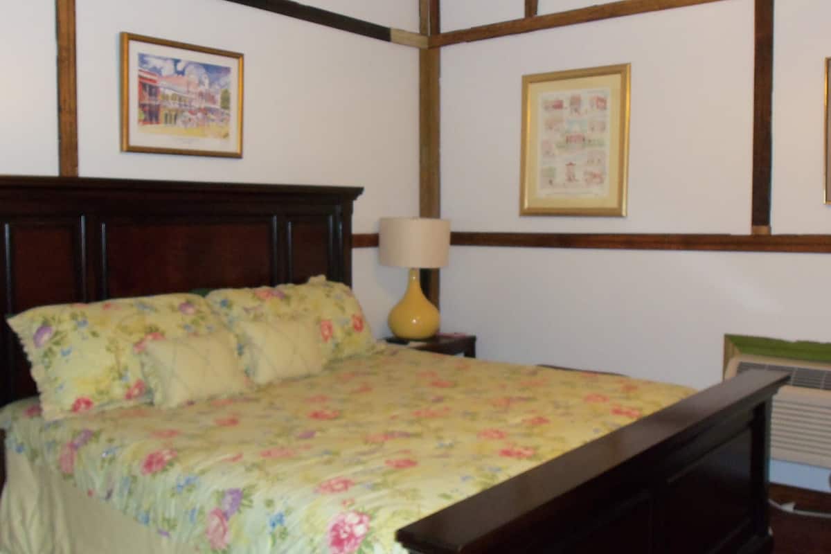 Ein Schlafzimmer mit einem Holzbettgestell, floralem Bettzeug, einem Nachttisch mit Lampe und gerahmten Bildern an der Wand.