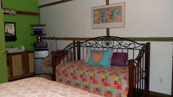 A bedroom with a bed, a nightstand, a dresser, a microwave, and a painting on the wall.