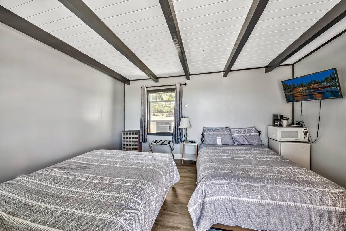 A room with two beds, a TV, a microwave, and a window with curtains.