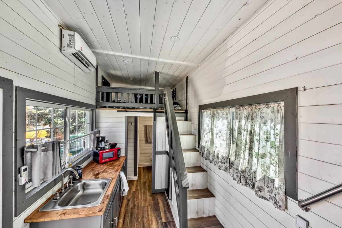 A compact kitchen with a wooden countertop, a built-in sink, and a red microwave. A staircase leads to an upper level.