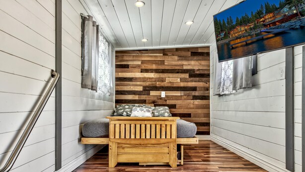A wooden bench with cushions in a hallway with a wooden wall and a painting of a lakeside scene. - West Walker Motel (Coleville)