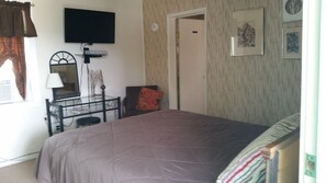 A bedroom with a bed, a desk with a chair, a television mounted on the wall, and a door. - West Walker Motel (Coleville)