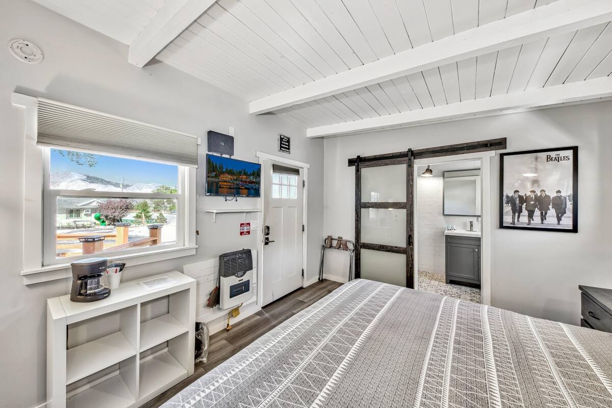 A hotel room with a large bed, a window with a view, a coffee machine, a painting, and a door leading to a bathroom.