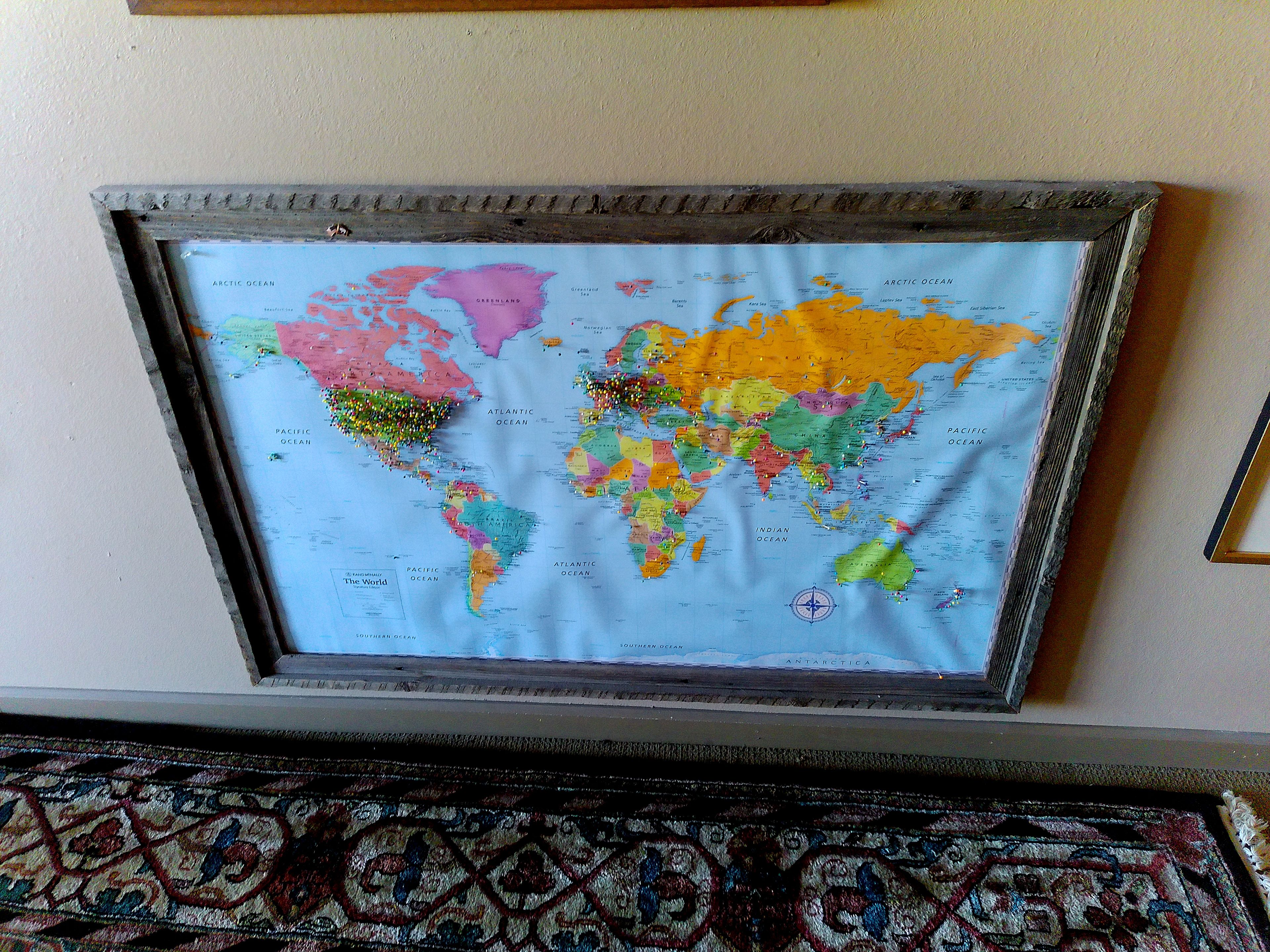 A framed world map with a compass rose, mounted on a wall.