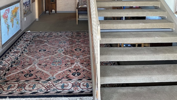 A staircase with a woven handrail, surrounded by framed artworks and a large patterned rug. - Rawlins Lodge (Rawlins)