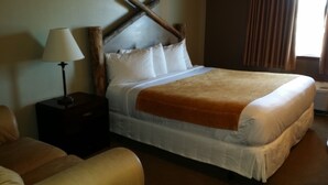 A hotel room with a large bed, a bedside table with a lamp, and a chair. - Rawlins Lodge (Rawlins)