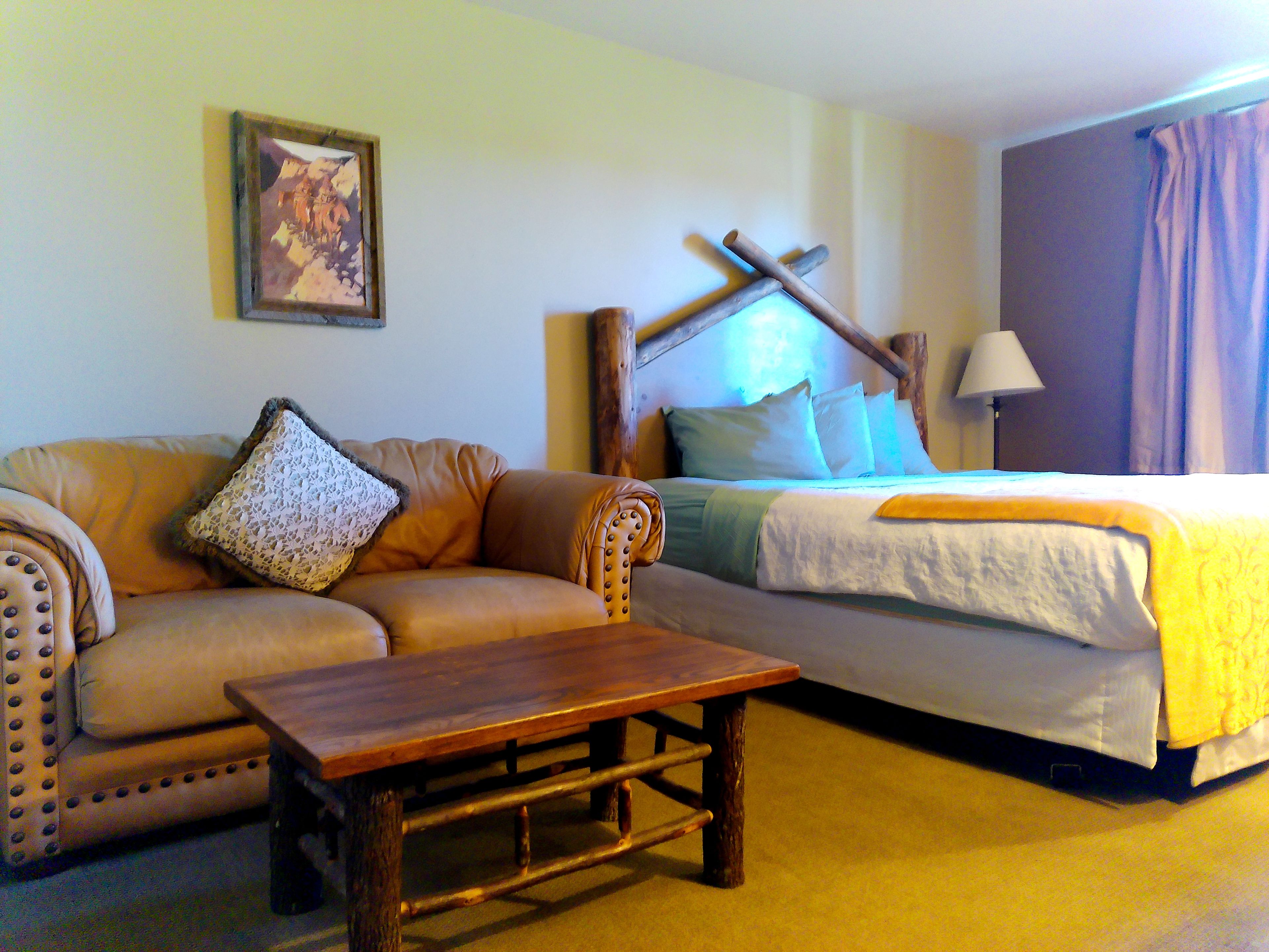 A room with a bed, a sofa, a wooden table, and a lamp.