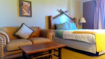 A room with a bed, a sofa, a wooden table, and a lamp.