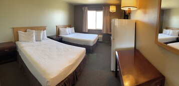 A hotel room with two single beds, a wooden nightstand, a desk, a refrigerator, and a window with curtains.