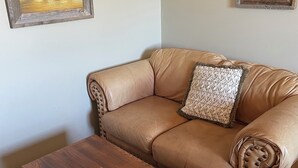 A tan leather sofa with a patterned throw pillow, a wooden coffee table, and two framed paintings on the wall. - Rawlins Lodge (Rawlins)