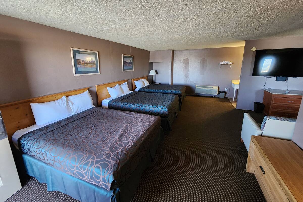 A hotel room with three beds, a TV, a desk, and a chair.
