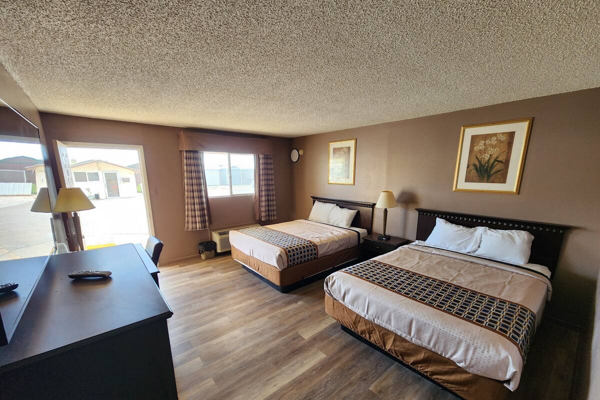 A hotel room with two beds, a desk, a chair, a lamp, and a window with curtains.