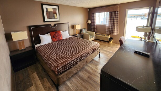 A hotel room with a bed, bedside tables, a desk, a chair, a window with curtains, and a ceiling with a speckled pattern.