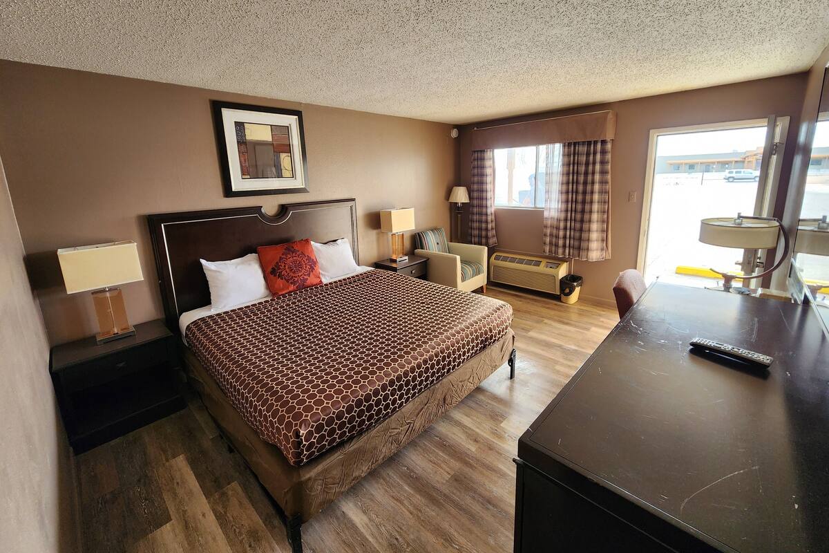 A hotel room with a bed, bedside tables, a desk, a chair, a window with curtains, and a ceiling with a speckled pattern.