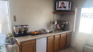 A kitchen with a tiled floor, wooden cabinets, a refrigerator, a coffee machine, and a television mounted on the wall.