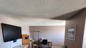 A hotel room with a flat-screen TV, wooden dresser, two chairs, a small table, and a framed picture on the wall.