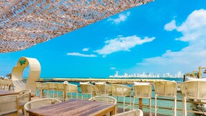 A seaside restaurant with wicker furniture and a view of the city skyline. - Palmarito Beach Hotel (Cartagena)