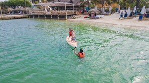 A beach with thatched-roof huts, a wooden pier, and lounge chairs on the sand. - Palmarito Beach Hotel (Cartagena)
