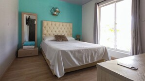 A bedroom with a tufted headboard, a large window with curtains, a bedside table, and a mirror. - Palmarito Beach Hotel (Cartagena)