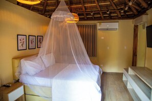 A bed with a canopy, a nightstand, a wall-mounted air conditioner, and framed botanical illustrations. - Palmarito Beach Hotel (Cartagena)