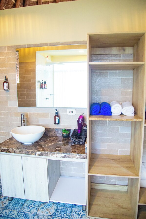 A bathroom with a white sink, a mirror, a shelf with towels, and toiletries. - Palmarito Beach Hotel (Cartagena)
