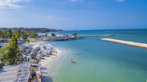 Una playa con filas de tumbonas y sombrillas, un rompeolas rocoso y aguas tranquilas.