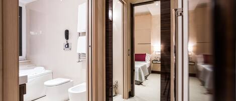 Un baño moderno con bañera, inodoro y lavamanos. Un espejo refleja una habitación con cama y mesa.