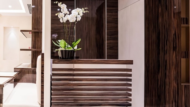 A modern interior with a wooden slatted partition, a potted orchid, and a white sofa. - Maison Candia Luxury House (Rome)