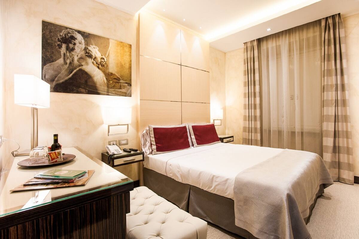 Una camera d'albergo con un letto, comodini, una scrivania, una sedia, un quadro appeso al muro e tende.