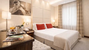 A hotel room with a large bed, a desk with a lamp, a painting on the wall, and a window with curtains. - Maison Candia Luxury House (Rome)