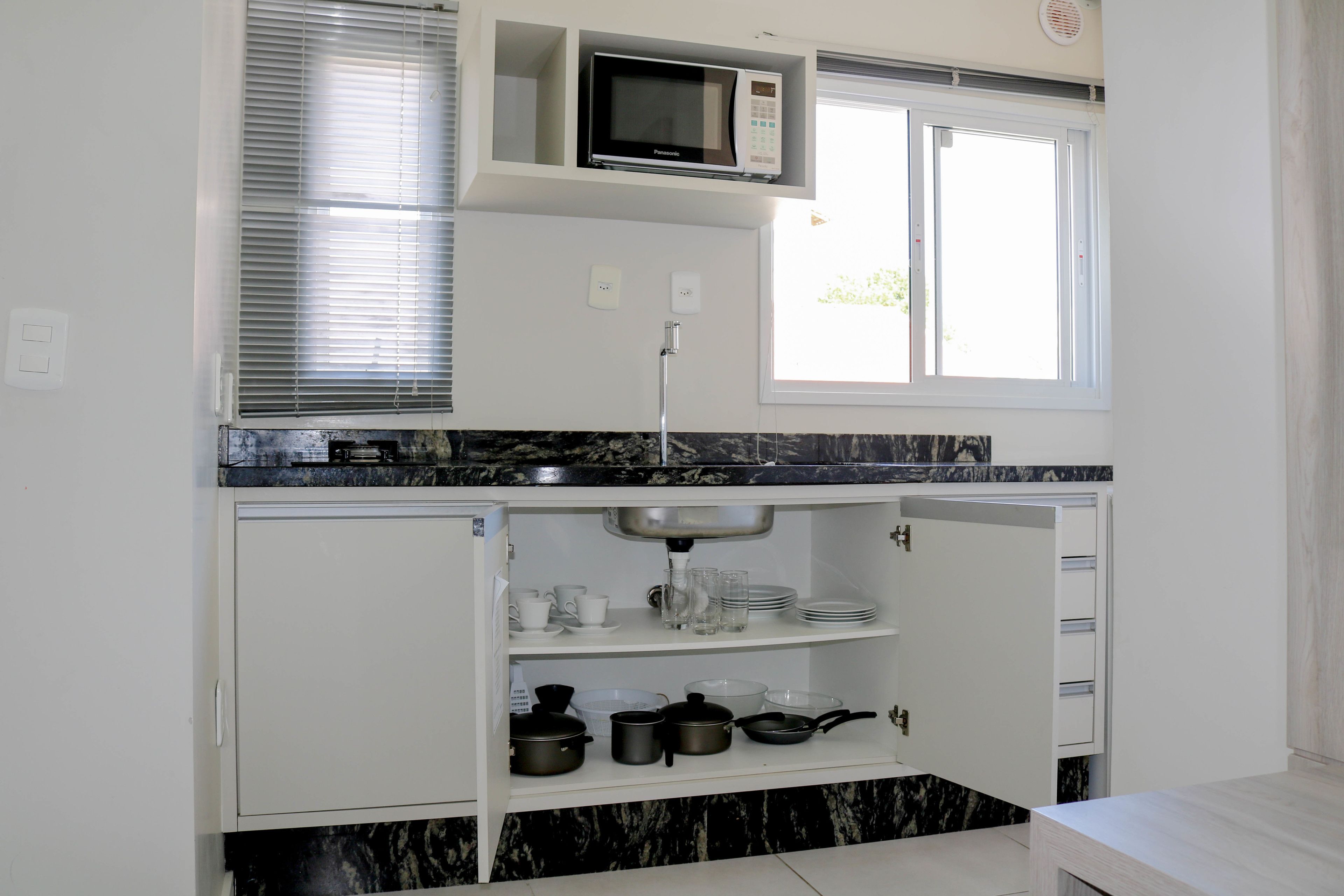 A compact kitchen with a built-in microwave, a window with blinds, and a sink area with dishes and cookware.