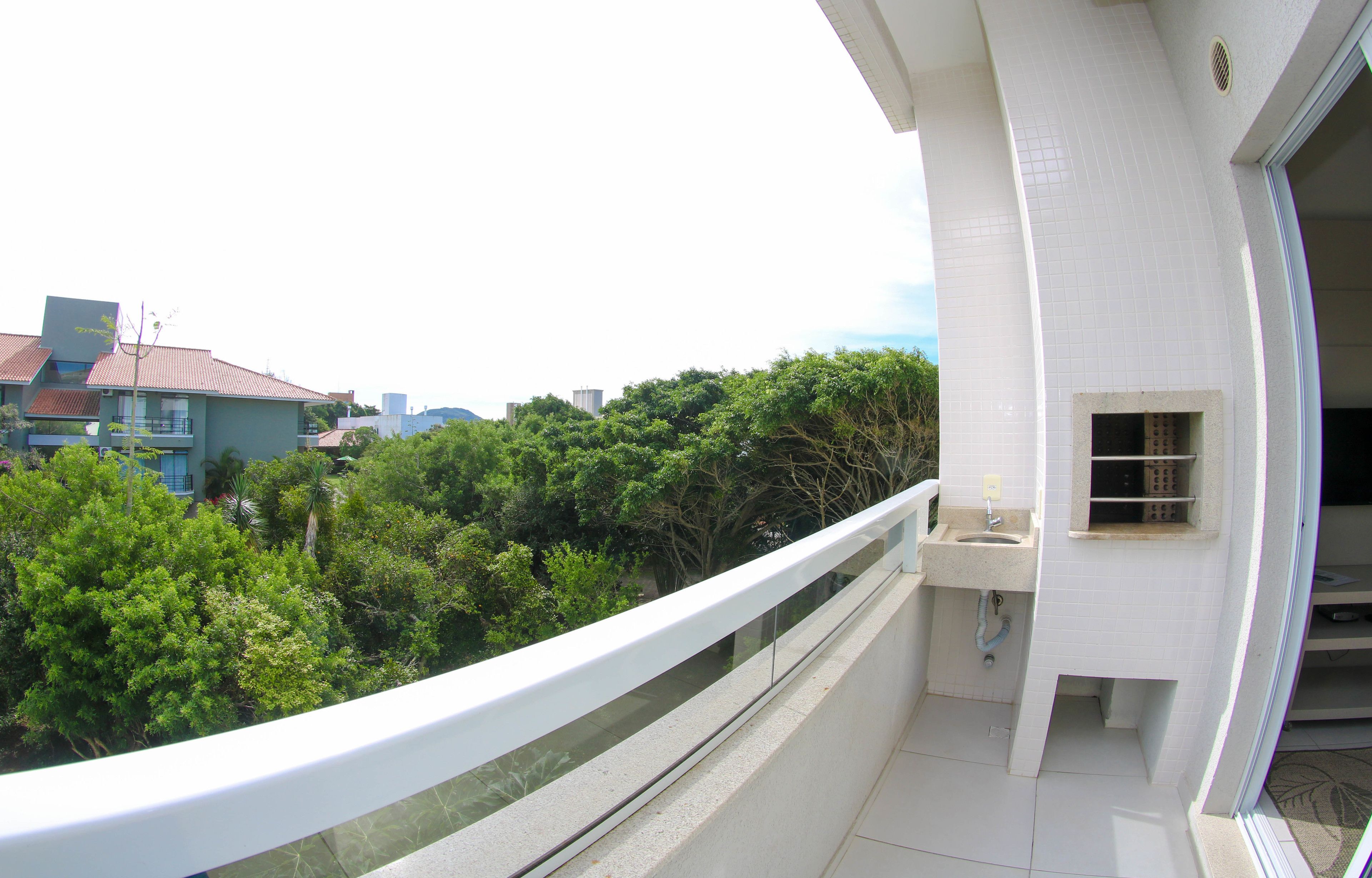 A balcony with a white railing overlooking a lush green area and a cityscape.