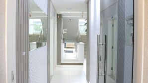 A modern hotel corridor with a glass shower enclosure, a central staircase, and a view of the outdoor area.