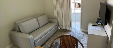 A living room with a sofa, a wooden dining table, wicker chairs, a TV, and an air conditioning unit.