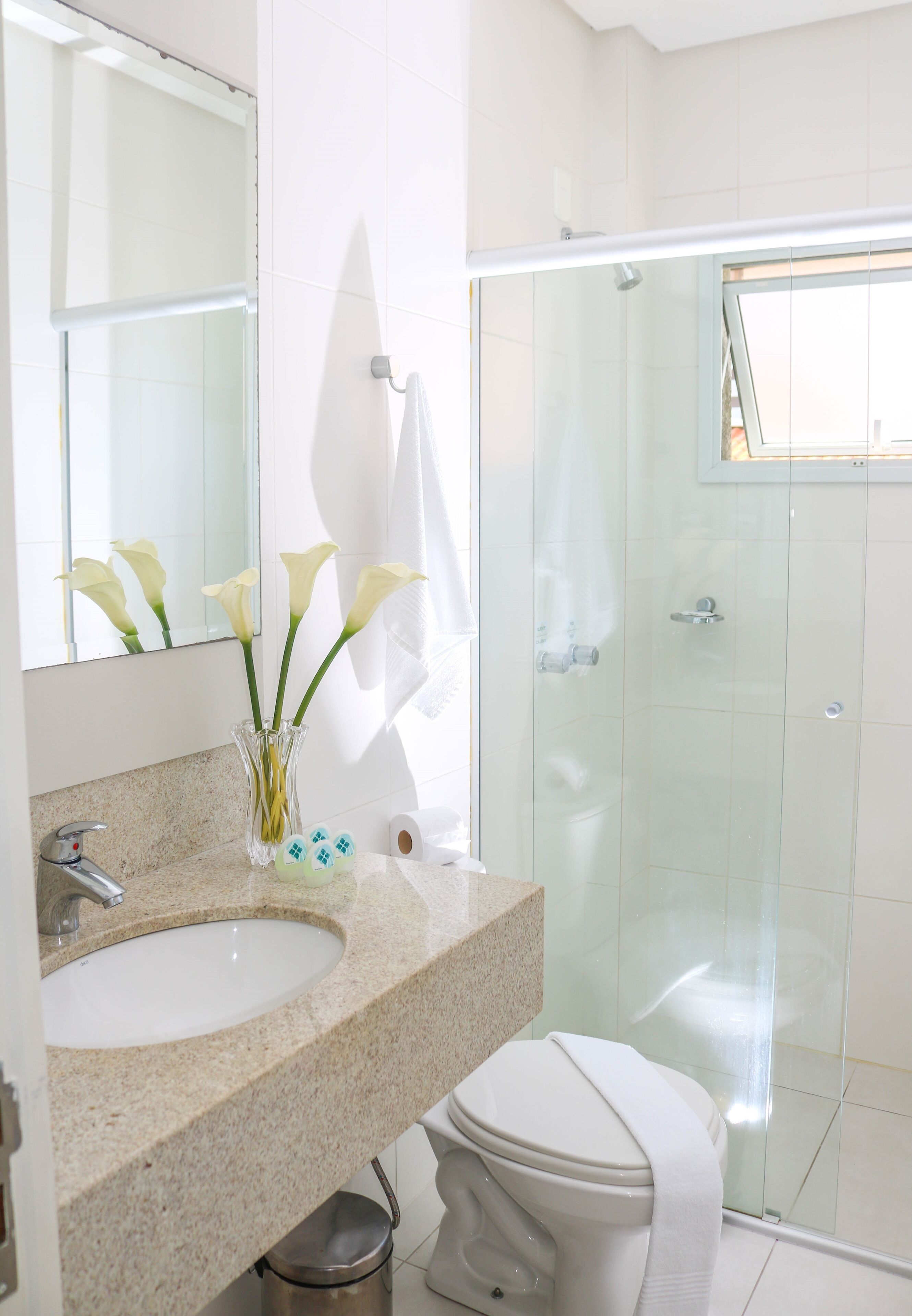 Un baño moderno con encimera de granito, un lavabo blanco, un espejo y una cabina de ducha con paredes de vidrio.